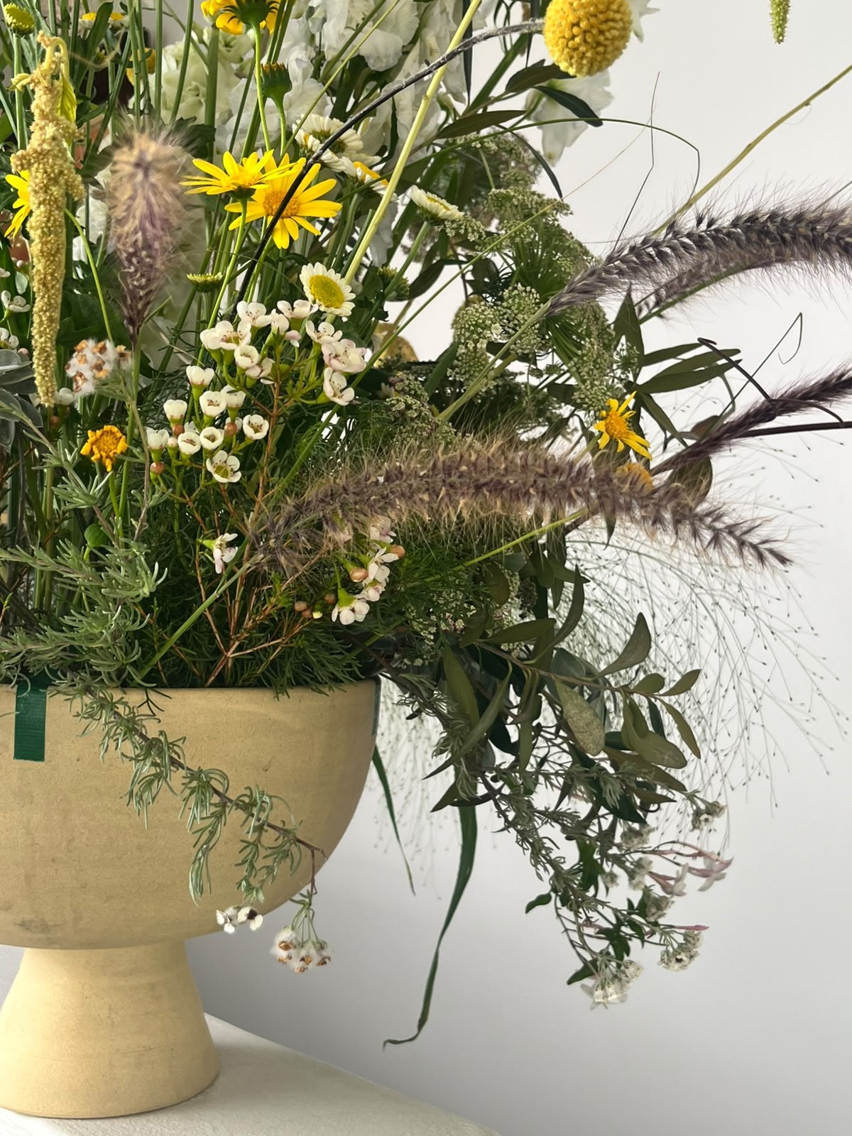 Wild field arrangement of daisies, wax flower and fountain grass in a stone vessel